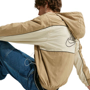 Person wearing a beige and white jacket with a brand logo, sitting on a light gray background