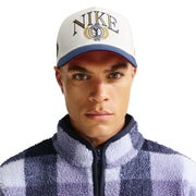 Person wearing a Nike cap and checkered jacket on a white background