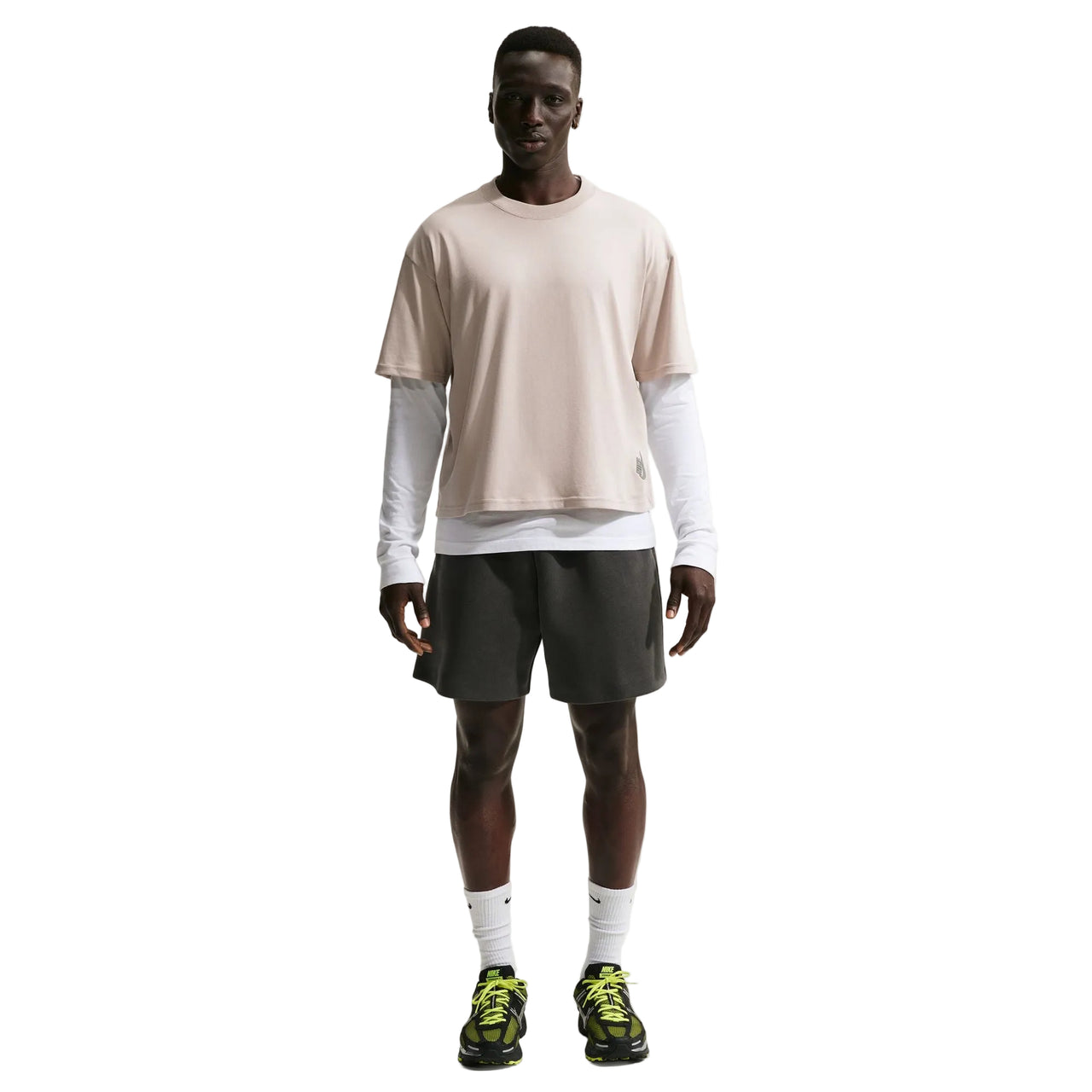 Man wearing a Nike beige t-shirt, gray shorts, and black sneakers on a white background