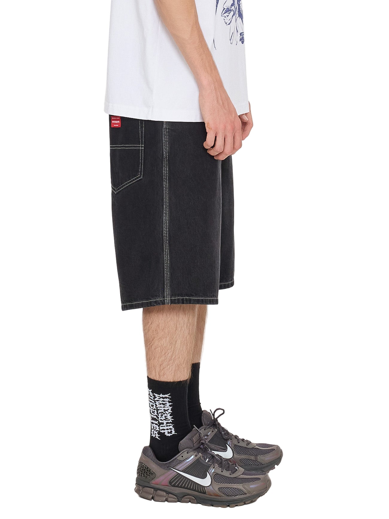 Person wearing black denim shorts, white t-shirt, and Nike shoes on a white background